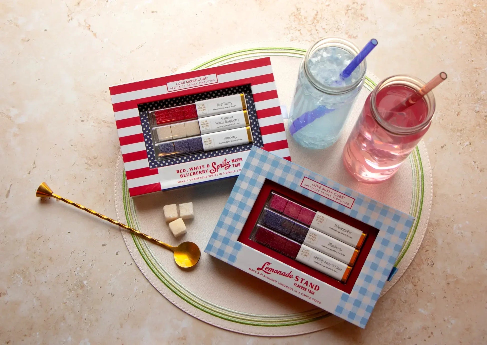 Two boxes of candy on a plate with two drinks and a spoon on a beige surface